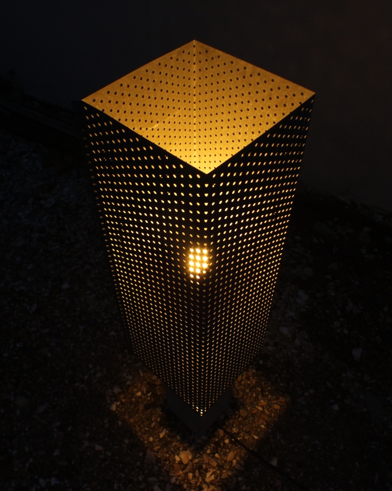 a closeup nightime photo of a lamp made of concrete and perforated sheet steel